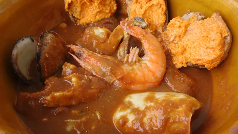 Bouillabaisse servie dans un plat en terre cuite avec crevettes, coquillages et croûtons à la rouille