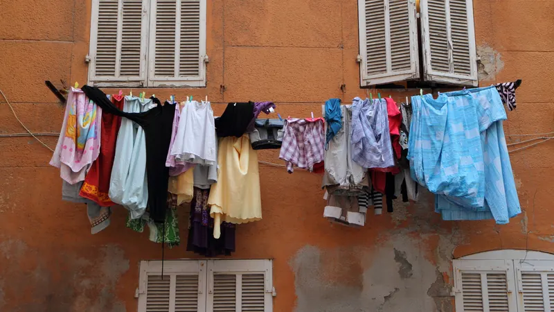 Linge coloré qui sèche entre deux fenêtres à volets sur une façade ocre du Panier, à Marseille