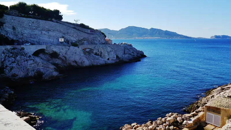 Crique d'eau turquoise et rochers blancs le long de la corniche Kennedy à Marseille, avec les îles au loin