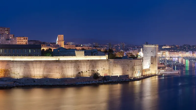 Le fort Saint-Jean illuminé de nuit à l'entrée du Vieux-Port de Marseille, sous un ciel bleu nuit