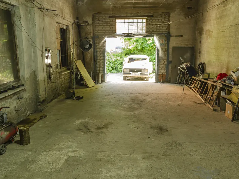 Atelier de garage automobile avec compresseur et établis, une voiture garée devant la porte ouverte