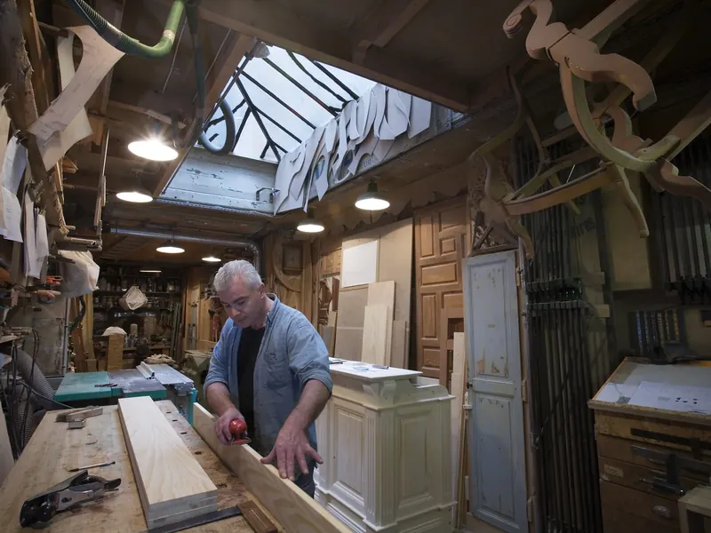 Menuisier au travail sur une planche dans un atelier rempli d'outils et de boiseries