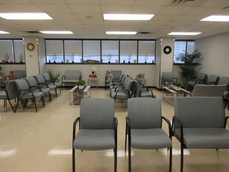 Grande salle d'attente d'un centre médical avec chaises grises et larges fenêtres